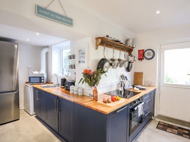 A kitchen with blue cabinets wooden countertops pots hanging on a rack and kitchen appliances at Silva in Penmon