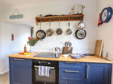 A kitchen with blue cabinets wooden countertop hanging pots and pans flowers knives and a stove at Silva in Penmon