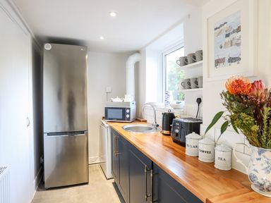A kitchen with a stainless steel refrigerator wooden countertop microwave sink and shelves with mugs at Silva Penmon
