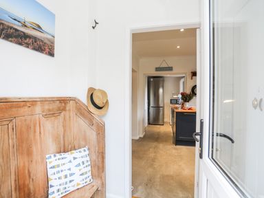 A hallway with wooden bench and hat hanging on wall leading to a kitchen with refrigerator and microwave at Silva in Penmon