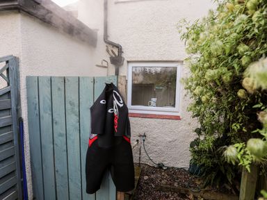 An outdoor shower area with a wetsuit hanging on a wooden fence and a window with a mug inside at Silva in Penmon