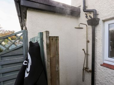An outdoor shower head and handheld shower next to a white textured wall and a wooden fence at Silva in Penmon