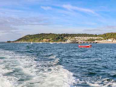 A coastal view with boats on the water and a small town with greenery in the background at Silva in Penmon
