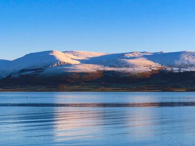 A body of water with mountains in the background with snow on them at Silva in Penmon