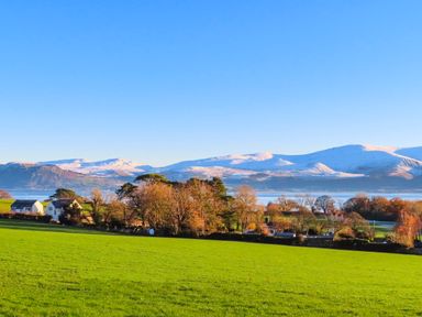 A green field with trees and houses in front of snow covered mountains at Silva in Penmon