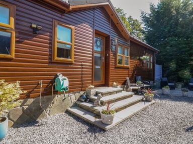 Exterior of a wooden house with steps leading to a door surrounded by planters and outdoor seating at RoseGrace Lodge in Auchterarder