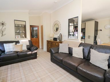 A living room with two dark sofas with cushions a wooden sideboard mirror and wall decoration at RoseGrace Lodge in Auchterarder