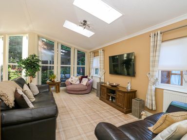 A living room with leather sofas a round chair a wooden TV stand and large windows at RoseGrace Lodge in Auchterarder