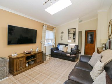 A living room with two leather sofas a wall mounted TV and a wooden TV stand at RoseGrace Lodge in Auchterarder
