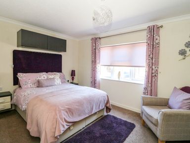 A bedroom with a double bed floral bedding curtains armchair and window at RoseGrace Lodge in Auchterarder
