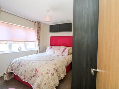 A bedroom with a double bed covered with butterfly patterned bedding next to a window with closed blinds and floral curtains at RoseGrace Lodge in Auchterarder