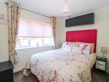 A bedroom with a bed featuring butterfly bedding and pink pillows next to a window with floral curtains at RoseGrace Lodge in Auchterarder
