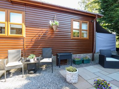 An outdoor seating area with black chairs and a small table next to a brown wooden building at RoseGrace Lodge in Auchterarder