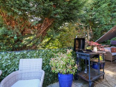 An outdoor patio area with a white wicker chair a barbecue grill and plants in blue pots at RoseGrace Lodge in Auchterarder
