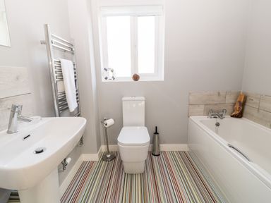 A bathroom with a sink towel rack toilet bathtub and striped floor at Seagull Cottage in Bude