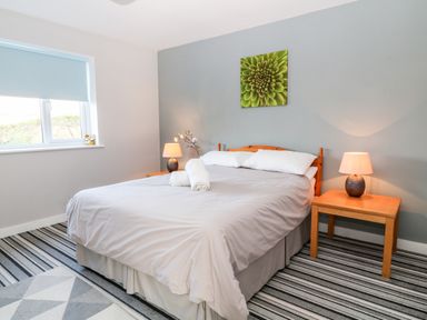A bedroom with a double bed two bedside tables with lamps a window and a green flower painting on the wall at Seagull Cottage in Bude