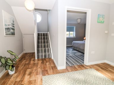 A hallway with wood flooring a striped carpeted staircase a potted plant and a bedroom visible through an open door at Seagull Cottage in Bude