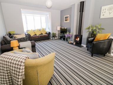A living room with striped carpet a wood stove black armchair two sofas and a yellow armchair at Seagull Cottage in Bude