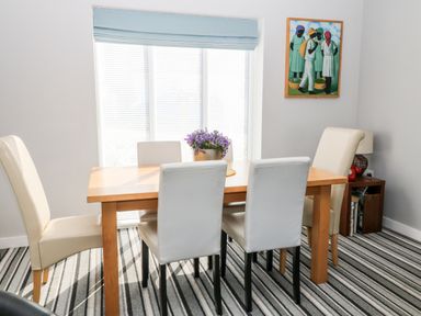 A dining room with a wooden table surrounded by six chairs and a flower centerpiece at Seagull Cottage in Bude