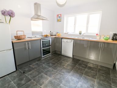A kitchen with grey cabinets a stove dishwasher refrigerator and a window at Seagull Cottage in Bude