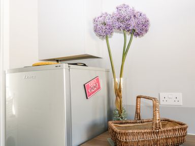 A kitchen corner with a refrigerator a vase with purple flowers and a wicker basket on the counter at Seagull Cottage in Bude