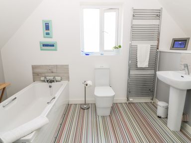 A bathroom with a bathtub toilet sink striped floor and a towel radiator at Seagull Cottage in Bude