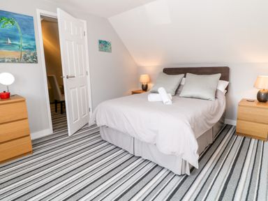 A bedroom with a double bed two bedside tables with lamps a chest of drawers and striped carpet at Seagull Cottage in Bude