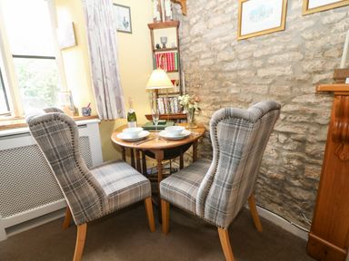 A dining area with two plaid chairs and a round wooden table set with bowls and cutlery at Coln Cottage in Stow-On-The-Wold