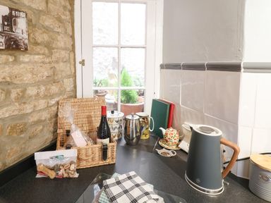 A kitchen counter with a wicker basket holding a bottle of wine and snacks near a kettle and teapot at Coln Cottage in Stow-On-The-Wold