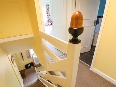 A staircase with white railing and wooden newel post leading to rooms with open doors at Coln Cottage in Stow On The Wold