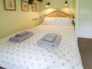A bedroom with a double bed with folded towels on it and framed pictures on the wall at Coln Cottage in Stow-On-The-Wold