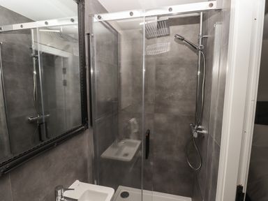 A bathroom with a glass shower enclosure a rainfall showerhead a handheld shower and a small sink at The Poppy Fields Abode in Dyserth