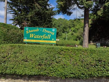 A green sign for Rhaeadr Dyserth Waterfall near bushes and trees at The Poppy Fields Abode in Dyserth