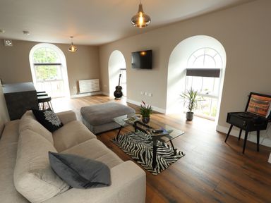 A living room with a sofa ottoman glass coffee table and guitar at The Poppy Fields Abode in Dyserth
