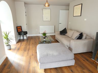 A living room with a beige sofa a glass coffee table with a plant and magazines a gray ottoman music player and a potted plant at The Poppy Fields Abode in Dyserth