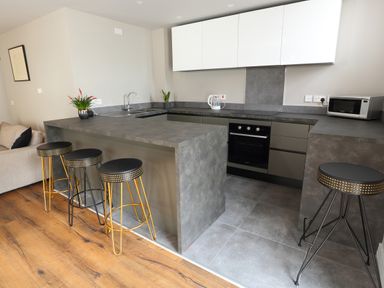 A modern kitchen with bar stools around a grey island and cabinets at The Poppy Fields Abode in Dyserth