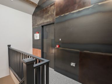 A hallway with a black railing a door and industrial style dark metal wall panels at The Sigma Penthouse in Dyserth