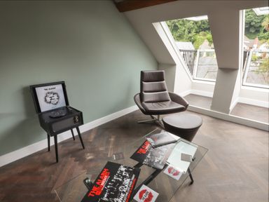 A room with a record player on a stand a leather chair with ottoman and a glass coffee table with vinyl records at The Sigma Penthouse in Dyserth