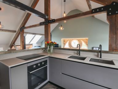 A kitchen area with a stovetop, oven, double sink, and bouquet of flowers in a vase on the counter at The Sigma Penthouse in Dyserth