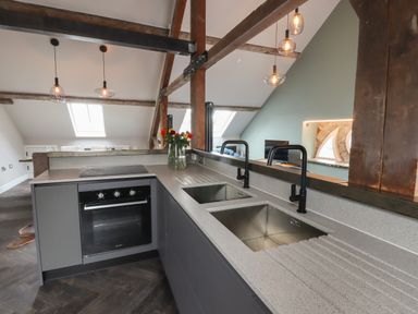 A kitchen with twin sinks, an oven, pendant lights, wooden beams and a vase with flowers at The Sigma Penthouse in Dyserth