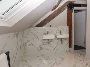A bathroom with two wall-mounted sinks and marble tiled walls and floor under a slanted ceiling at The Sigma Penthouse in Dyserth