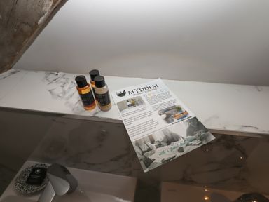 A bathroom counter with small bottles of toiletries and a leaflet on a marble surface at The Sigma Penthouse in Dyserth