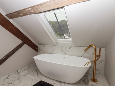 A bathroom with a freestanding bathtub under a skylight and a gold faucet at The Sigma Penthouse in Dyserth