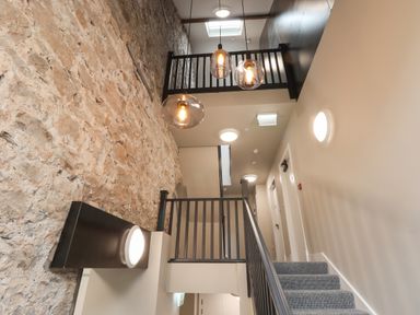 A stairway with carpeted steps and black railings next to a brick wall and hanging light fixtures at The Sigma Penthouse in Dyserth