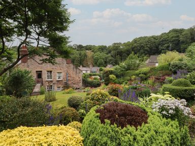 A garden with various bushes flowers and trees behind a stone house at The Sigma Penthouse in Dyserth