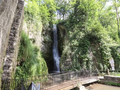 A waterfall surrounded by trees and rocks with a metal railing bridge in the foreground at The Sigma Penthouse in Dyserth