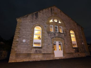 Exterior stone wall of a building with arched windows and a door illuminated at night at The Sigma Penthouse in Dyserth