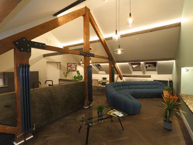 A living room with a blue curved sofa a glass coffee table and wooden beams on the ceiling at The Sigma Penthouse in Dyserth