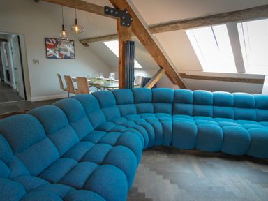 A curved blue sofa in a room with exposed wooden beams skylights and a dining table with chairs at The Sigma Penthouse in Dyserth