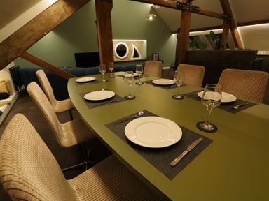 A dining area with a green table set with plates glasses and cutlery and beige chairs in a room with wooden beams at The Sigma Penthouse in Dyserth